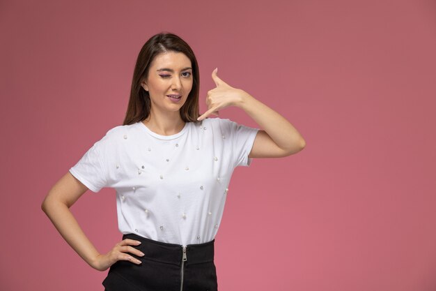 Mulher jovem de camisa branca, vista frontal, piscando e posando na parede rosa, cor mulher posar modelo mulher