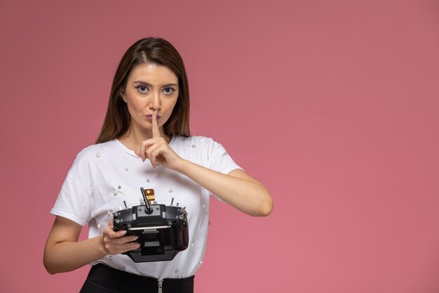 Mulher jovem de camisa branca, vista frontal, segurando o controle remoto na parede rosa, cor mulher modelo mulher