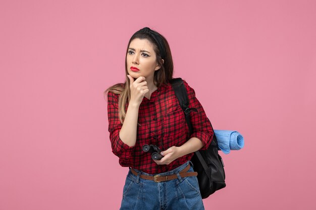 Mulher jovem de camisa vermelha com binóculos na mesa cor-de-rosa de frente