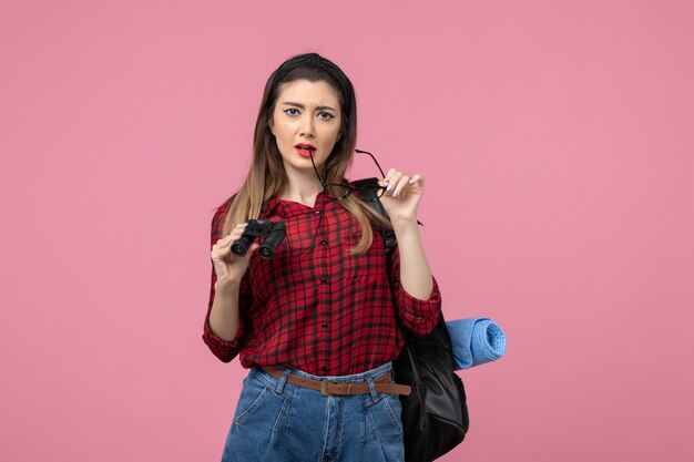 Mulher jovem de camisa vermelha com binóculos no modelo de cor de mulher de fundo rosa