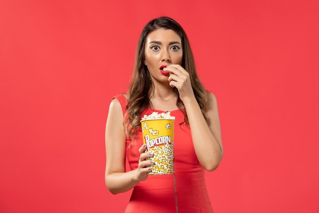 Mulher jovem de camisa vermelha comendo pipoca assistindo filme na mesa vermelha