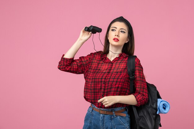 Mulher jovem de camisa vermelha usando binóculos em fundo rosa estudante cor de frente