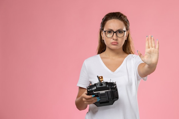 Mulher jovem de camiseta branca segurando o controle remoto no fundo rosa