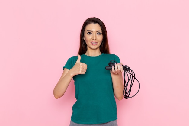 Mulher jovem de camiseta verde segurando a corda de pular na parede rosa claro cintura esporte exercícios exercícios beleza atleta magro de frente