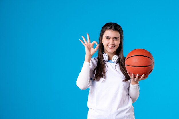 Mulher jovem de frente com basquete na parede azul