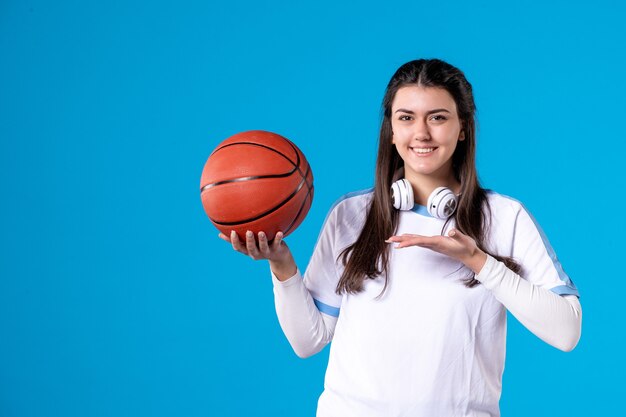 Mulher jovem de frente com basquete na parede azul