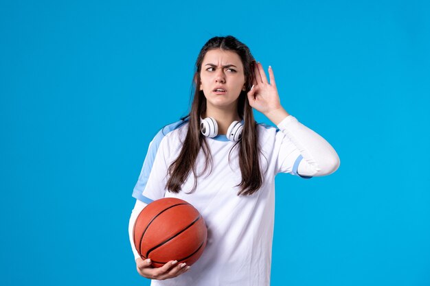 Mulher jovem de frente com basquete na parede azul