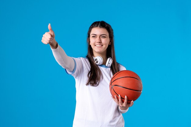 Mulher jovem de frente com basquete na parede azul