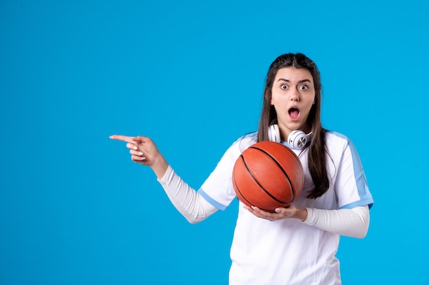 Mulher jovem de frente com basquete na parede azul