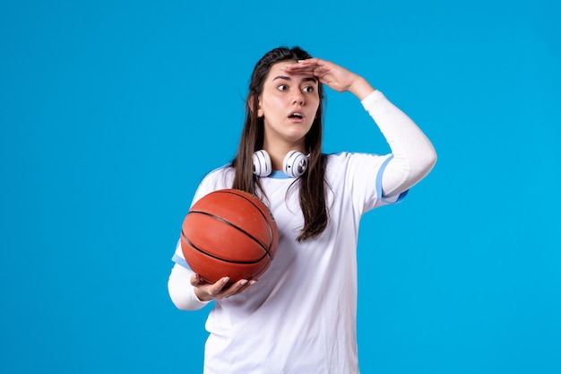 Mulher jovem de frente com basquete na parede azul