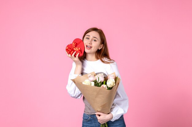 Mulher jovem de frente com flores e presente como presente de dia das mulheres em fundo rosa horizontal março igualdade feminino data rosas amor sensual