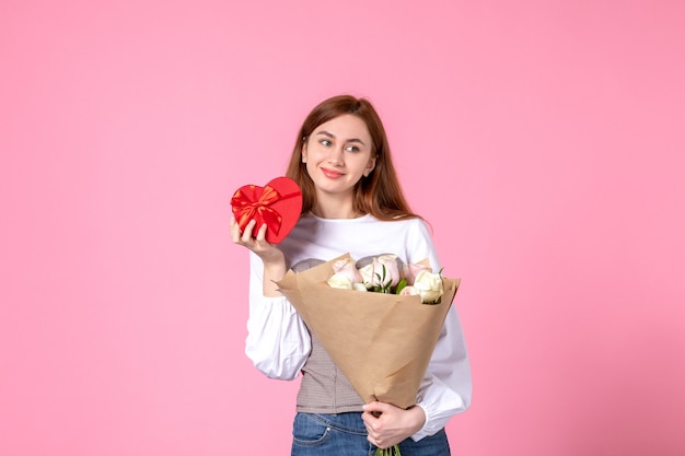 Foto grátis mulher jovem de frente com flores e presente como presente de dia das mulheres em fundo rosa horizontal março igualdade sensual feminino data rosa amor