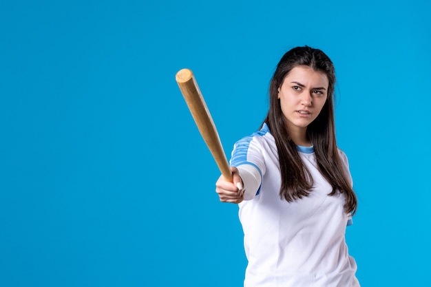 Mulher jovem de frente com taco de beisebol na parede azul