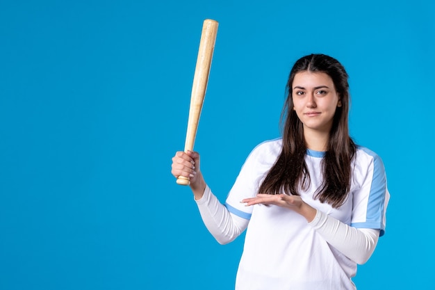 Mulher jovem de frente com taco de beisebol na parede azul