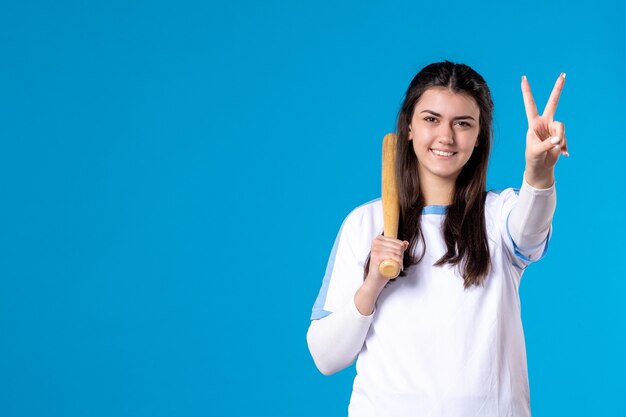 Mulher jovem de frente com taco de beisebol na parede azul