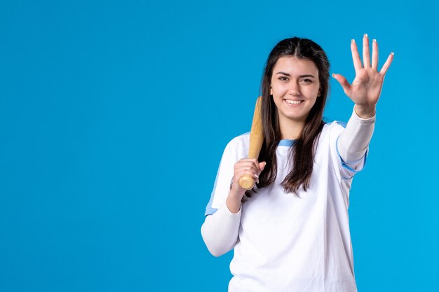 Mulher jovem de frente com taco de beisebol na parede azul