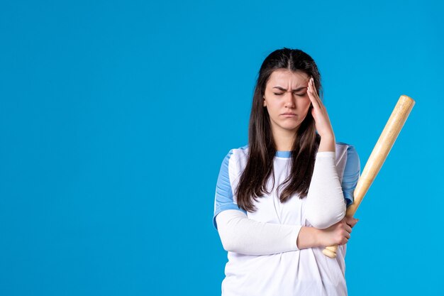 Mulher jovem de frente com taco de beisebol na parede azul