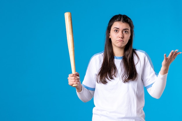 Mulher jovem de frente com taco de beisebol na parede azul