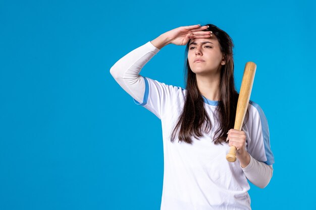 Mulher jovem de frente com taco de beisebol na parede azul