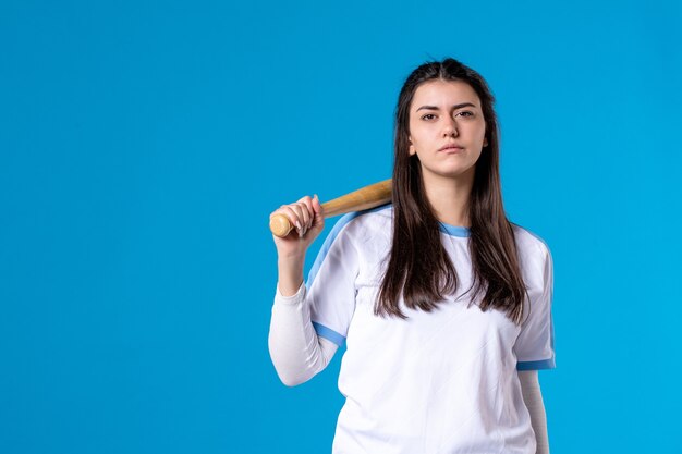 Mulher jovem de frente com taco de beisebol na parede azul