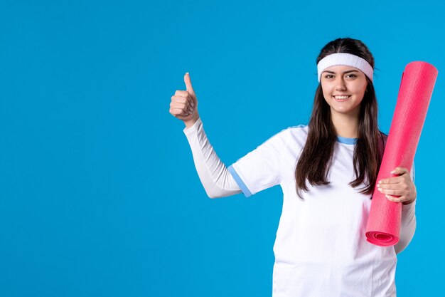 Mulher jovem de frente com tapete para exercícios na parede azul