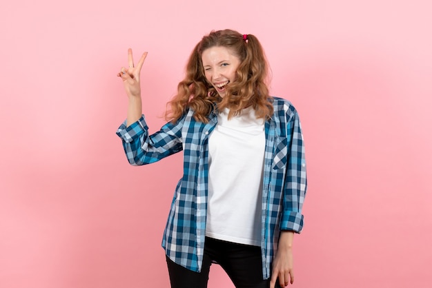 Mulher jovem de frente com uma camisa quadriculada azul com uma expressão feliz no fundo rosa.