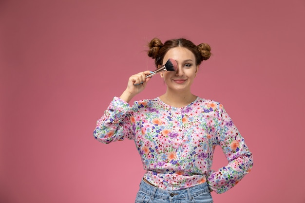 Mulher jovem de frente para a camisa com design floral e jeans azul, segurando a escova e sorrindo contra a luz de fundo