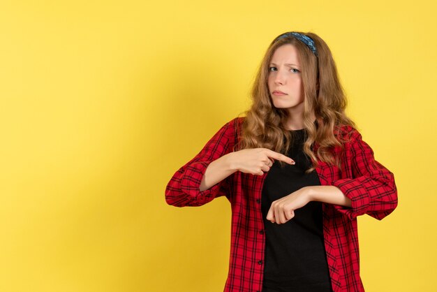 Mulher jovem de frente para a camisa quadriculada vermelha apontando o pulso no fundo amarelo modelo feminino cor de mulher