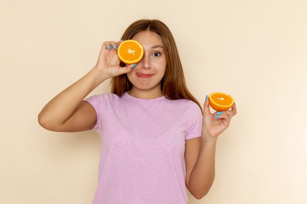 Mulher jovem de frente para a camiseta rosa e jeans azul segurando pedaços de laranja