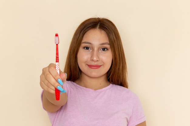 Mulher jovem de frente para a camiseta rosa e jeans azul segurando uma escova de dentes e sorrindo