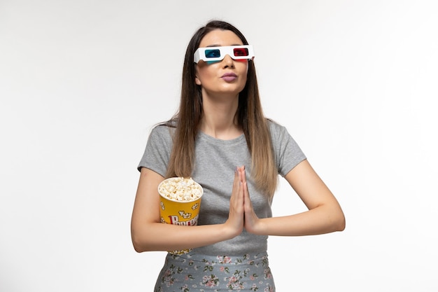 Mulher jovem de frente para comer pipoca e assistir filme com óculos de sol na mesa branca