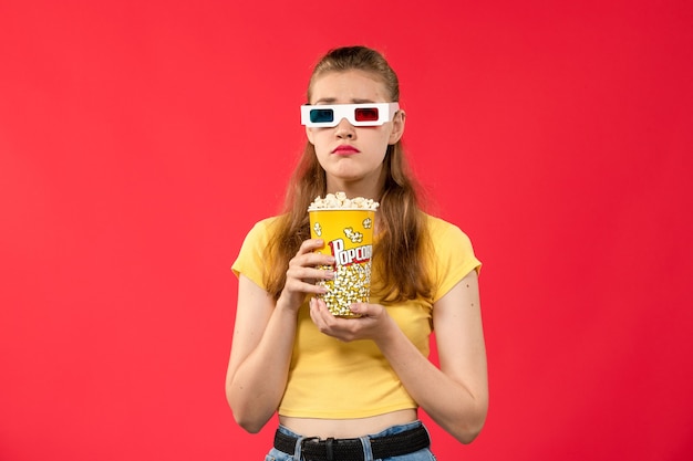 Mulher jovem de frente para o cinema segurando pipoca em d óculos de sol na parede vermelha.