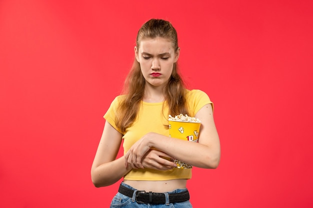 Mulher jovem de frente para o cinema segurando um pacote de pipoca e estressada na parede vermelha filmes teatro cinema lanche divertido filme