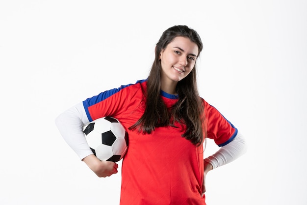 Mulher jovem de frente para o esporte com uma bola de futebol na parede branca