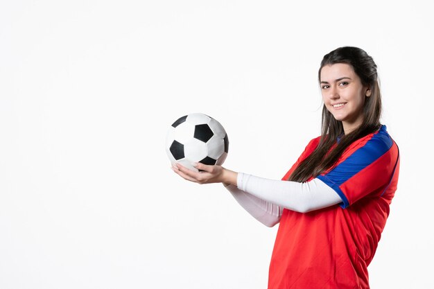 Mulher jovem de frente para o esporte com uma bola de futebol na parede branca