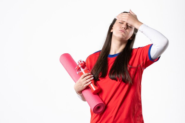 Mulher jovem de frente para o esporte em roupas esportivas com tapete de ioga e parede branca