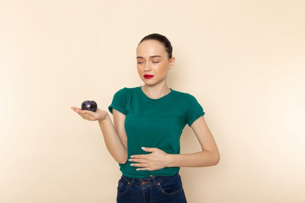 Mulher jovem de frente para uma camisa verde escura e jeans azul, com dor de estômago devido a ameixa azul em bege