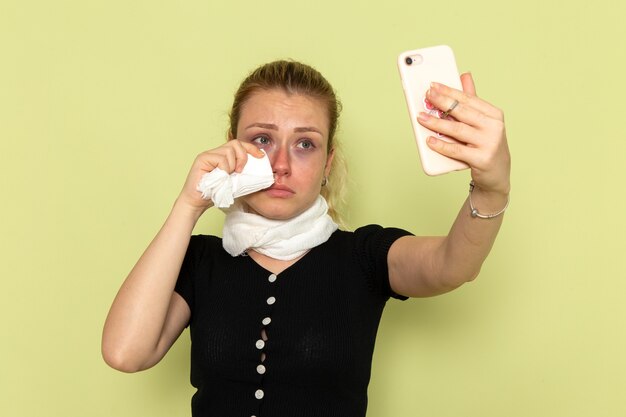 Mulher jovem, de frente, se sentindo muito doente e doente, tirando uma selfie na parede verde