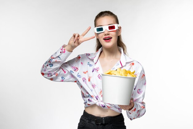 Mulher jovem, de frente, segurando a cesta com batatas fritas em óculos de sol d na superfície branca