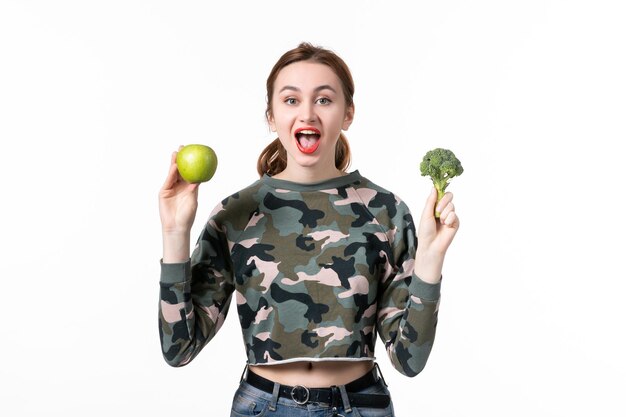 Mulher jovem de frente segurando maçã verde e brócolis no fundo branco pele horizontal suco fruta humana bem-estar
