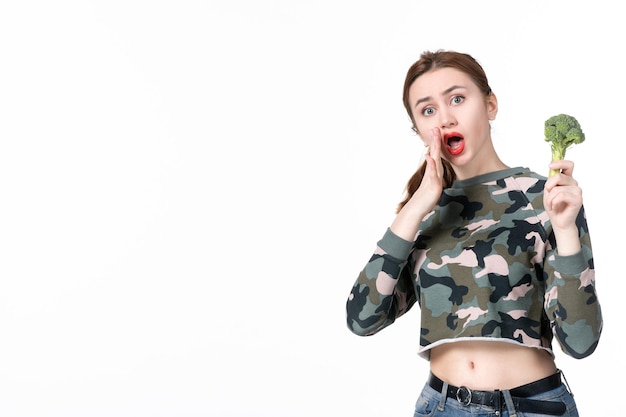 Foto grátis mulher jovem, de frente, segurando um pequeno brócolis verde no fundo branco refeição salada prato almoço dieta saúde humana alimentação saúde peso