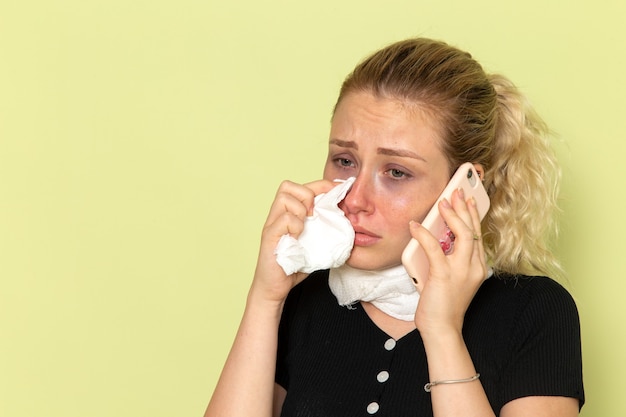 Mulher jovem, de frente, sentindo-se muito mal e doente, falando ao telefone na parede verde.