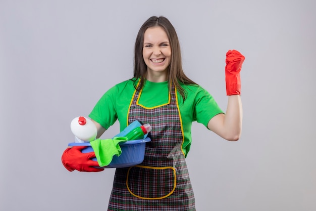 Foto grátis mulher jovem de limpeza alegre vestindo uniforme com luvas vermelhas segurando ferramentas de limpeza, mostrando um gesto de sim na parede branca isolada