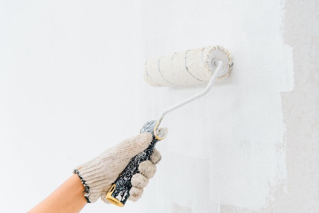 Mulher jovem de mãos pintando as paredes com um rolo usando tinta branca.