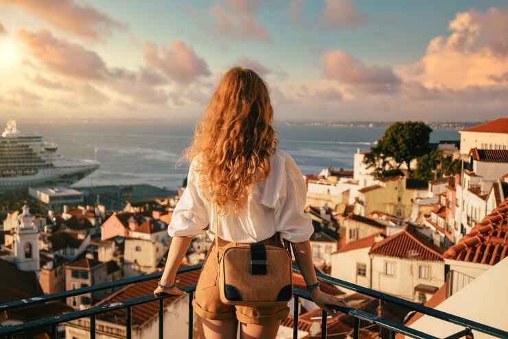 Foto grátis mulher jovem de pé numa plataforma cercada por cercas e observando lisboa durante o dia em portugal