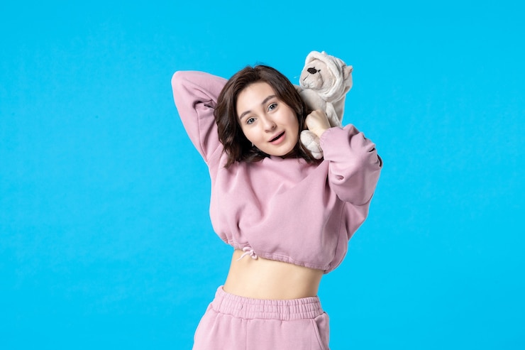 Foto grátis mulher jovem de pijama rosa com ursinho de brinquedo azul, vista frontal