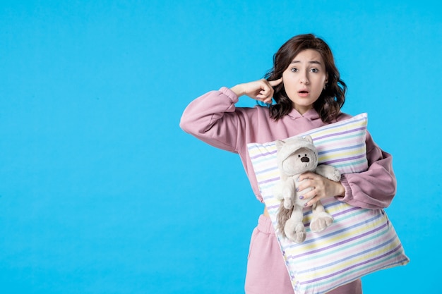 Mulher jovem de pijama rosa com urso de brinquedo e travesseiro azul de frente