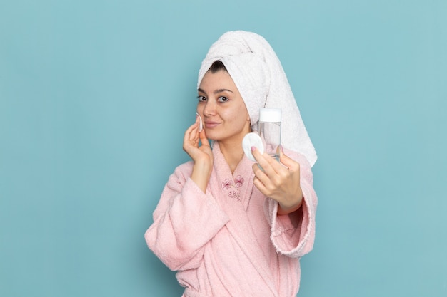 Foto grátis mulher jovem de roupão rosa segurando spray na parede azul de frente.