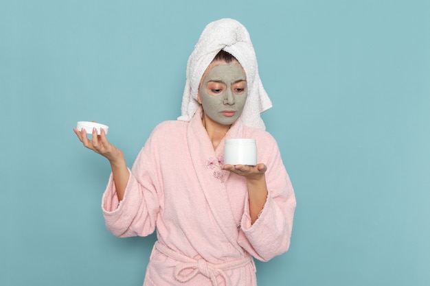 Mulher jovem de roupão rosa segurando uma lata de creme na parede azul.