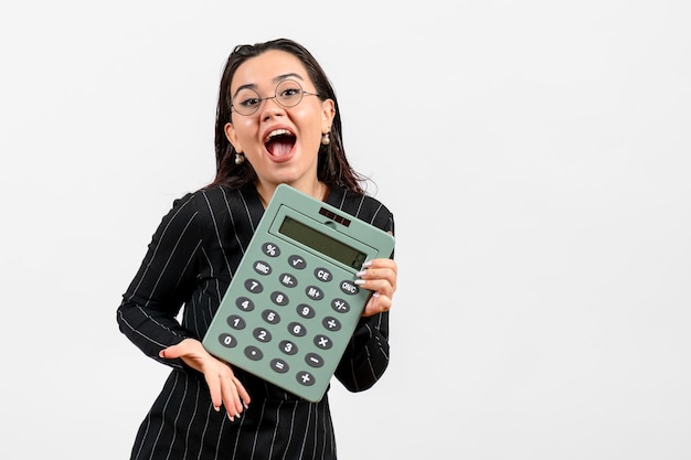 Foto grátis mulher jovem de terno escuro segurando uma calculadora grande no fundo branco.